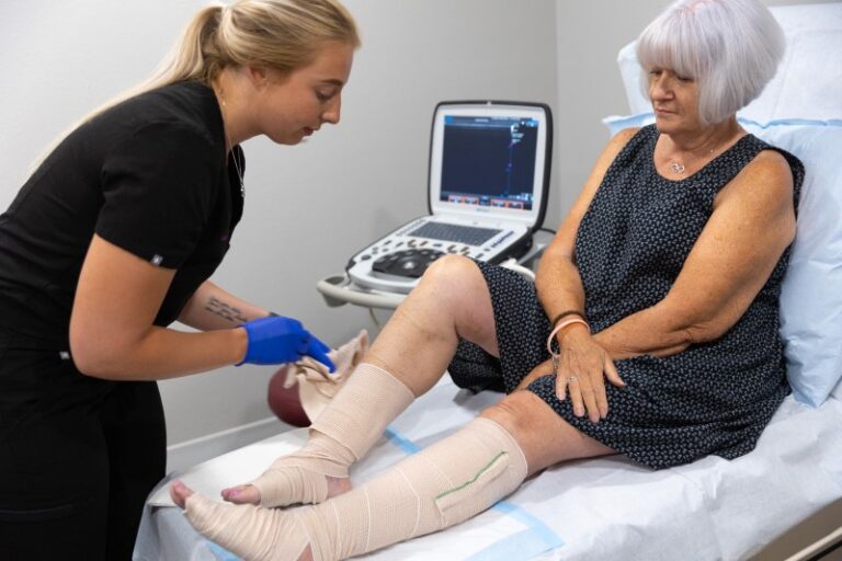 A mature woman laying on a treatment bed getting compression bandages put on her legs for leg pain at night in Venice, FL