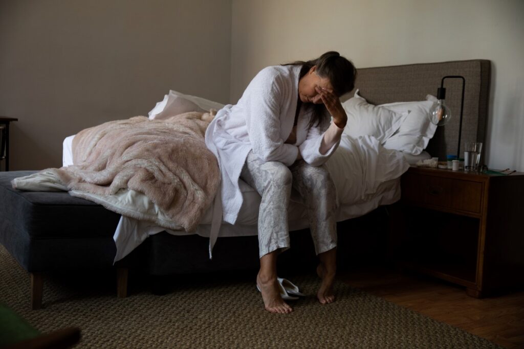 Mature woman sitting on the edge of her messy bed, seeming to be in pain after having leg pain at night in Venice, FL.